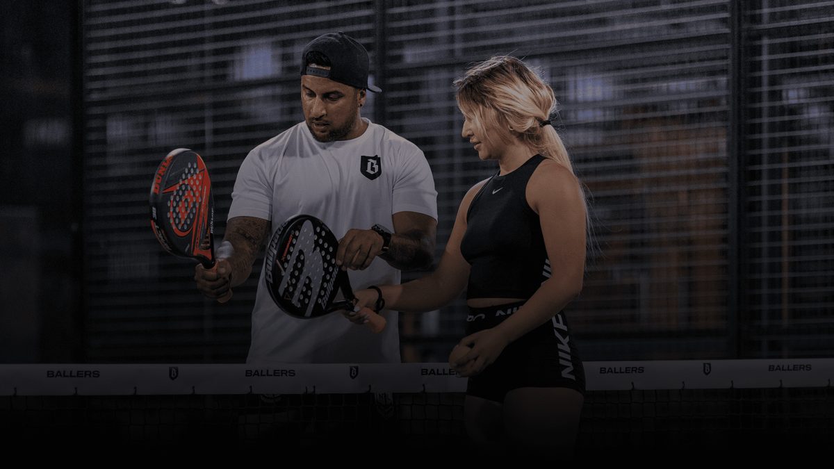 Two padel players with rackets courtside under floodlights